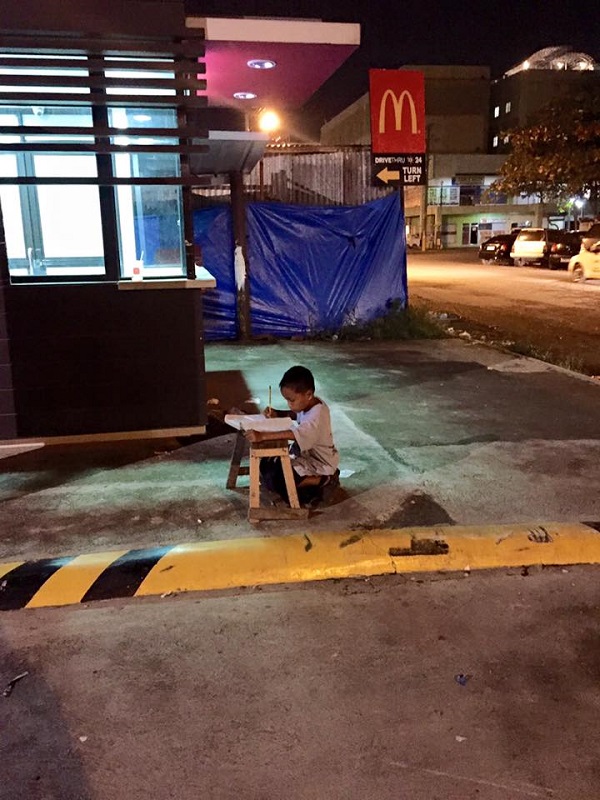El niño filipino hace sus deberes en la calle, iluminado por una farola